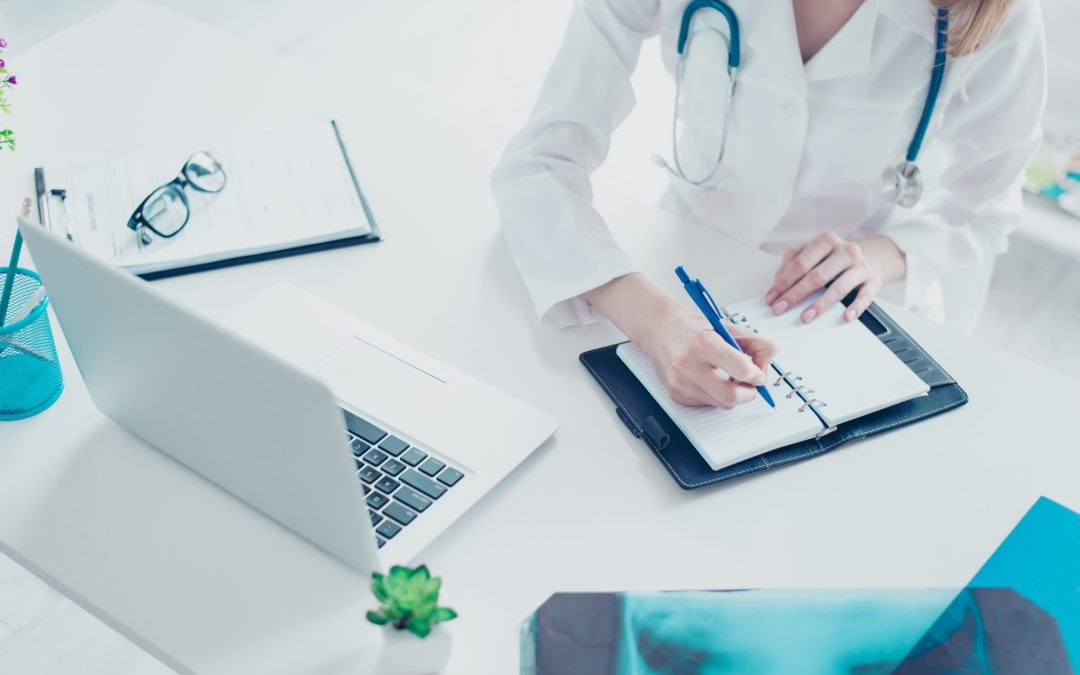 A doctor taking notes and listening to a patient during a telehealth appointment.